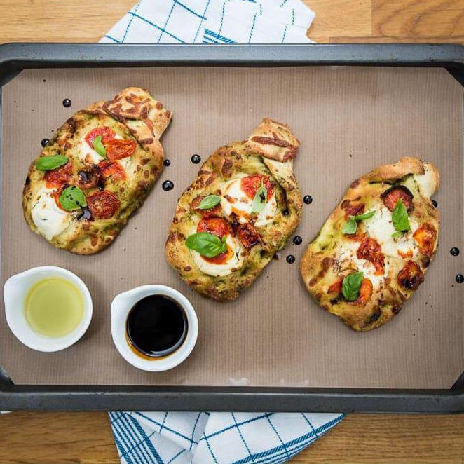 Three tomato, mozzarella and basil flatbread pizzas on a reusable non-stick Bake-O-Glide® liner in a baking tray