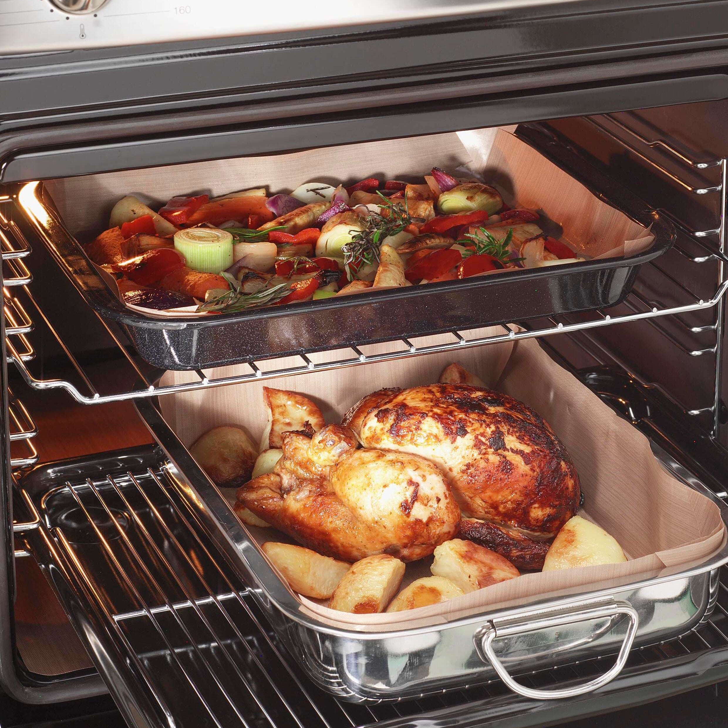 Two oven shelves with roasting tins lined with a Bake-O-Glide® liner, holding roast vegetables and a roast chicken