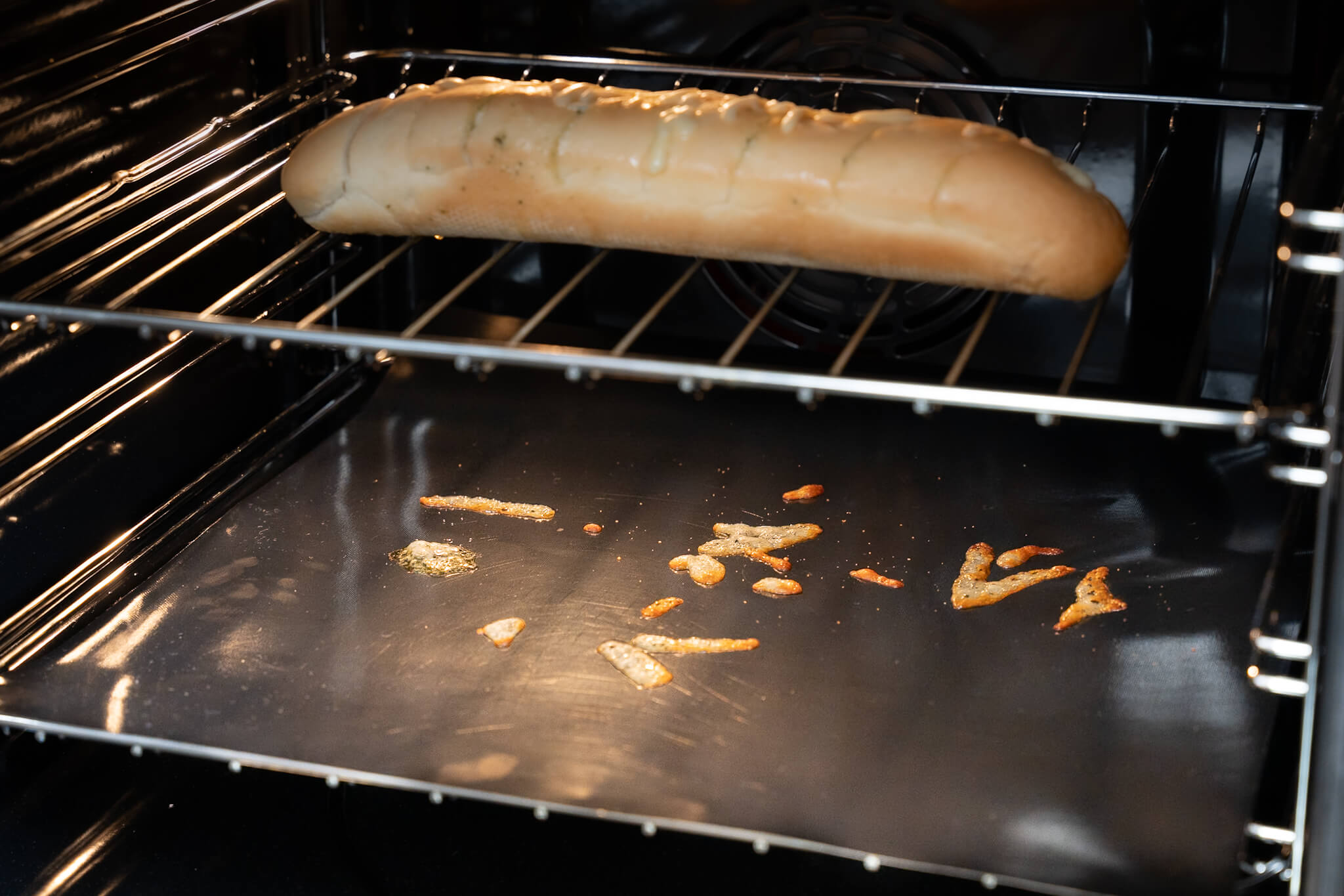 Extra Thick Oven liner catching spilt cheese from a garlic bread.